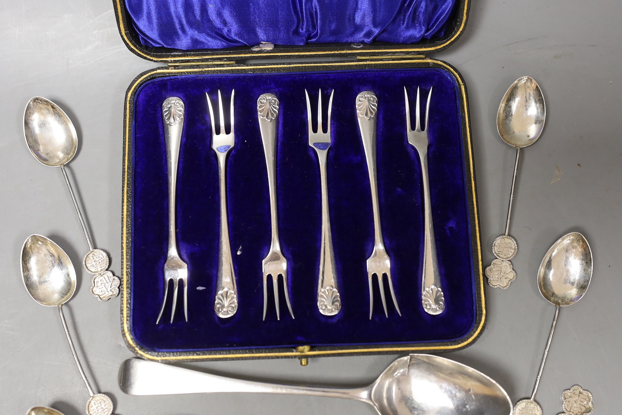 A cased set of six George V silver cake forks, a set of eleven Chinese white metal coffee spoons, a Georgian silver dessert spoon and a pair of white metal sugar tongs.